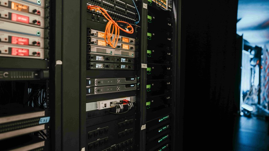  Ένα rack σε server room, γεμάτο με δικτυακό εξοπλισμό και εξοπλισμό ήχου, με πολλά ορατά καλώδια, συμπεριλαμβανομένου ενός πορτοκαλί καλωδίου patch.