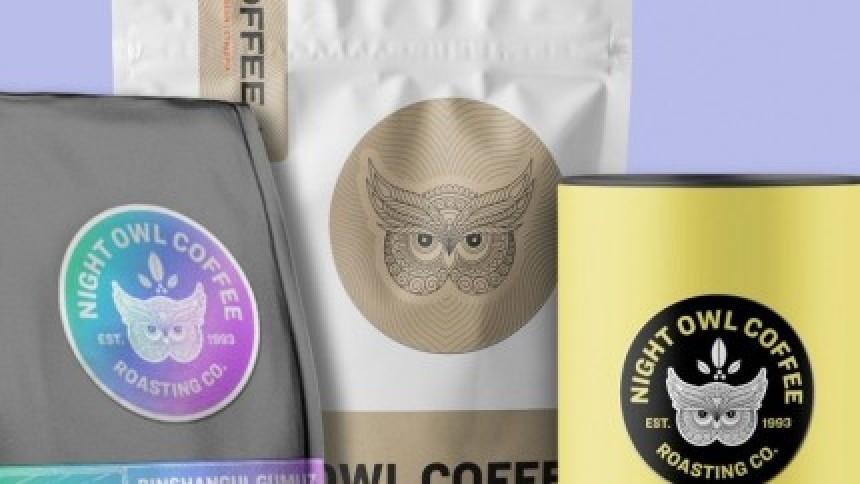 Τρεις διαφορετικές συσκευασίες καφέ 'Night Owl Coffee' που επιδεικνύουν τη χρήση ετικετών σε διάφορα υλικά: μια γκρι σακούλα με ολογραφικό αυτοκόλλητο, μια λευκή σακούλα με αυτοκόλλητο από χαρτί κραφτ, και ένα κίτρινο κουτί με μαύρο αυτοκόλλητο.
