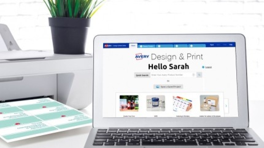 Ένα laptop με ανοιχτή την ιστοσελίδα του λογισμικού Avery Design & Print, δίπλα σε έναν εκτυπωτή που εκτυπώνει ένα φύλλο εξατομικευμένων ετικετών. Στην οθόνη φαίνεται η διεπαφή του προγράμματος.