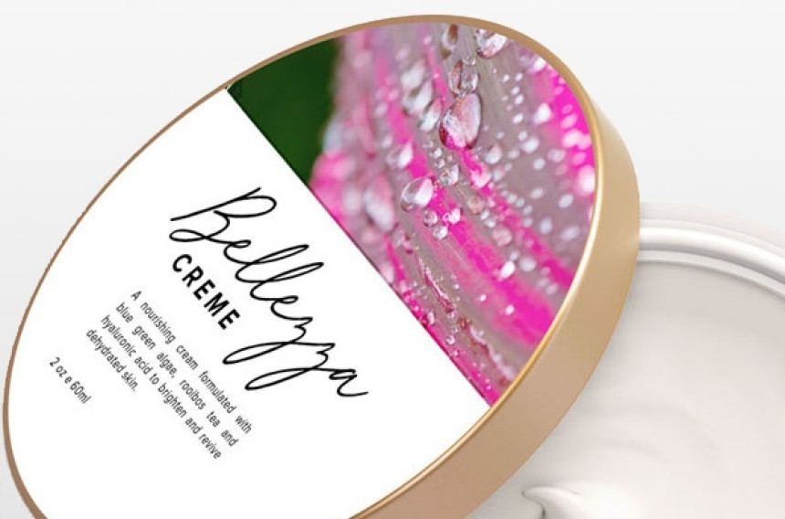 Κοντινό πλάνο σε ένα ανοιχτό βαζάκι με λευκή καλλυντική κρέμα. Στο καπάκι με τη χρυσή μπορντούρα υπάρχει μια ετικέτα με την επιγραφή 'Bellezza CREME' και μια φωτογραφία ενός ροζ λουλουδιού με σταγόνες δροσιάς.