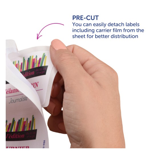 Η εικόνα δείχνει ένα χέρι που κρατά ένα φύλλο προκομμένων ετικετών σχεδιασμένο για εύκολη αποκόλληση. Η ετικέτα διαθέτει πολύχρωμα γραφικά και κείμενο που υποδεικνύουν λεπτομέρειες σχετικά με μια εκδήλωση.