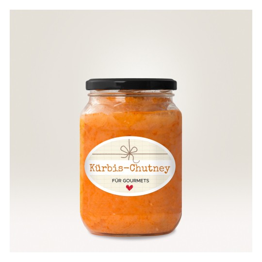 Η εικόνα δείχνει ένα βαζάκι Kürbis-Chutney με μια διακοσμητική ετικέτα. Το τσάτνεϊ έχει ένα ζωηρό πορτοκαλί χρώμα και το βαζάκι έχει μαύρο καπάκι. Η ετικέτα περιέχει το κείμενο 'Kürbis-Chutney für Gourmets' σε ένα ανοιχτόχρωμο φόντο.